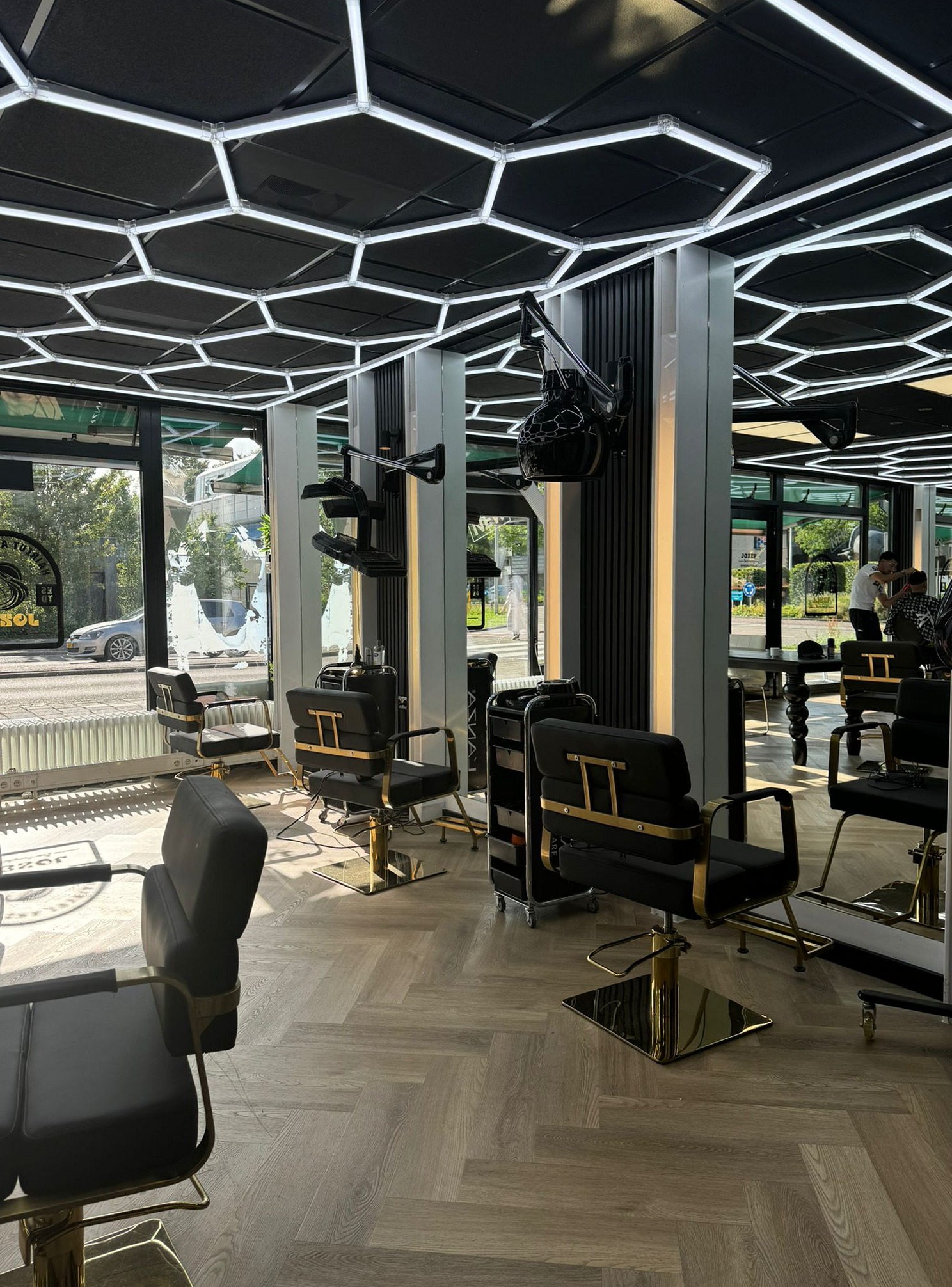 Het interieur van Jozef barbershop: zwarte stoelen met goud, een visgraatvloer en een plafond van zeshoekige lampen