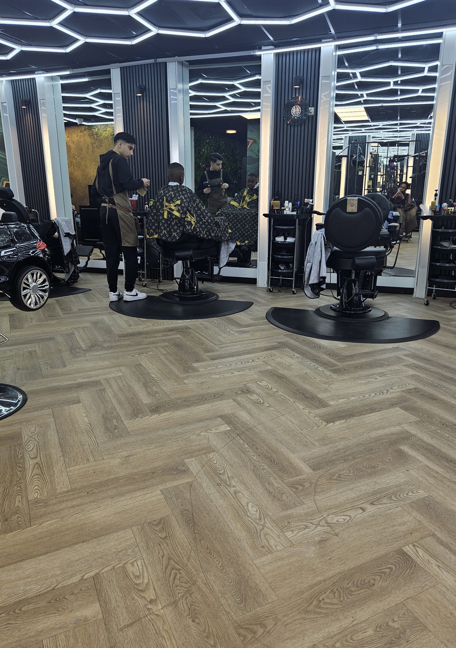 Barbers aan het werk in de zaak, onder het plafond van zeshoekige lampen